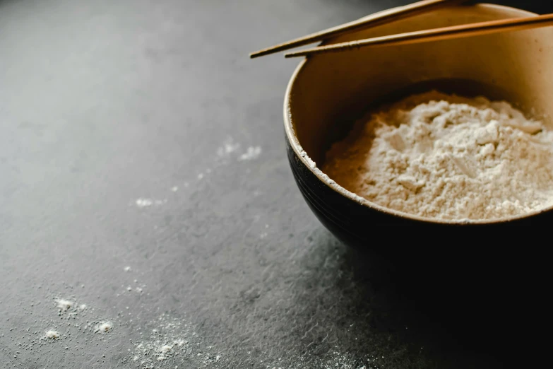 a close up of a bowl of food with chopsticks, unsplash, process art, flour dust, background image, bakery, grey