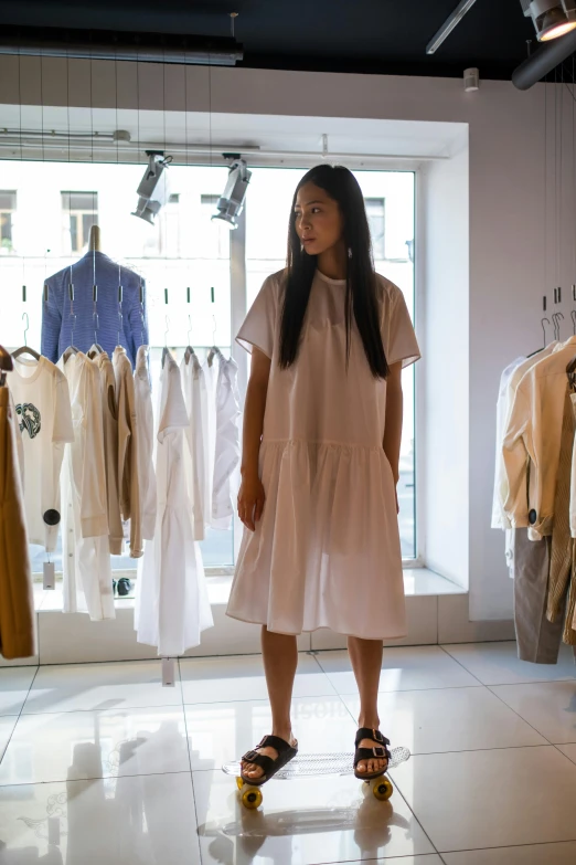 a woman standing in front of a rack of clothes, unsplash, gutai group, wearing a white hospital gown, tokyo fashion, showcase, like a catalog photograph