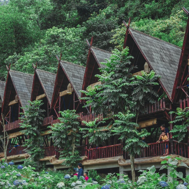 a group of people standing in front of a building, inspired by Yosa Buson, pexels contest winner, sumatraism, cottage in the forest, maroon, lush green, panoramic shot