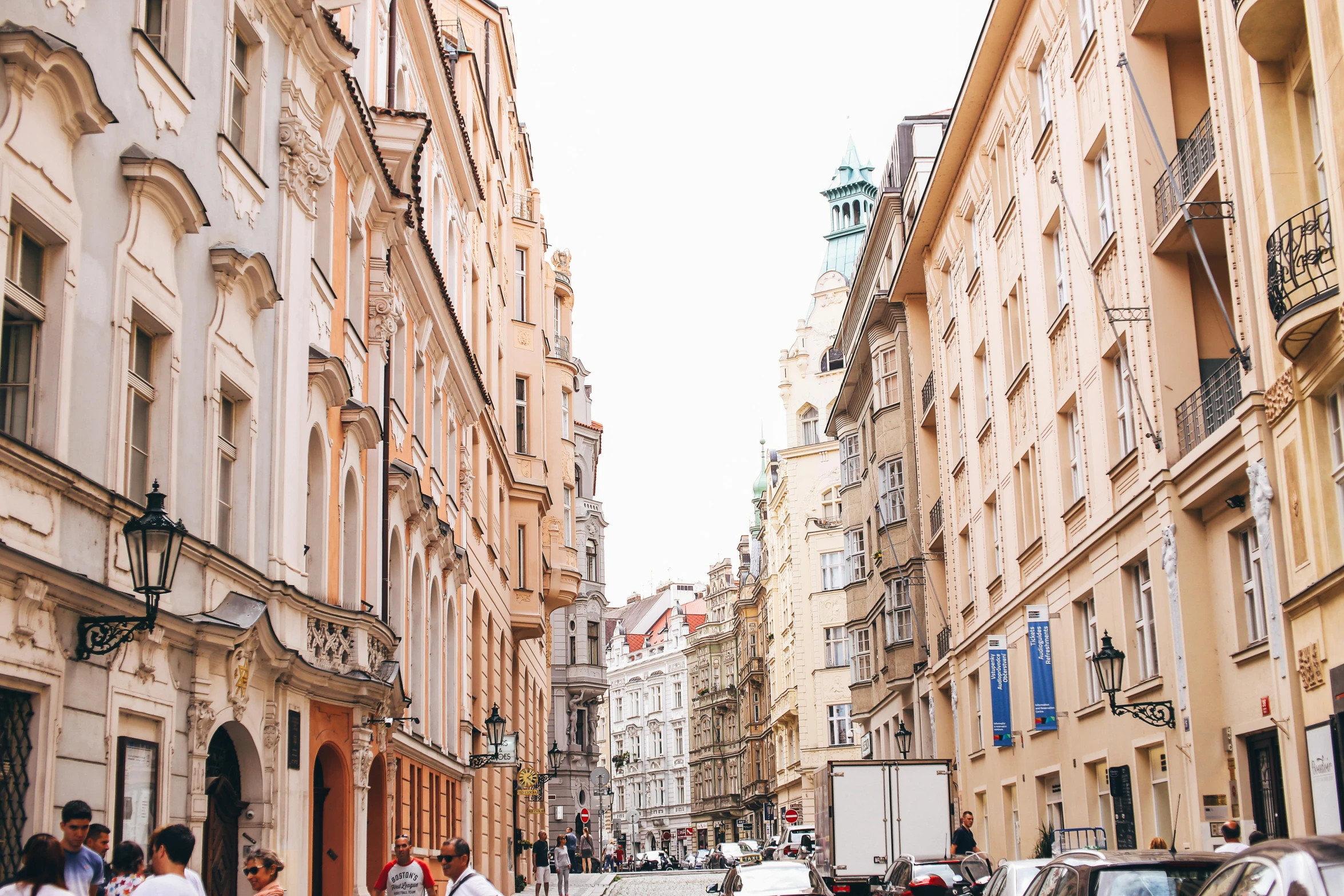 a group of people walking down a street next to tall buildings, by Emma Andijewska, pexels contest winner, art nouveau, prague, whitewashed buildings, 🦩🪐🐞👩🏻🦳, square