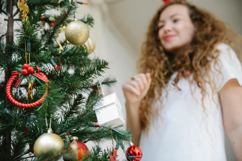 a woman standing next to a christmas tree, pexels contest winner, happening, long brown puffy curly hair, ornament, gif, white