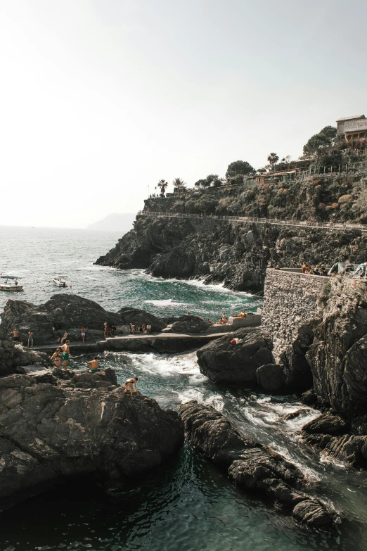 a group of people swimming in a body of water, by Carlo Martini, pexels contest winner, the village on the cliff, rocky coast, slide show, low quality photo