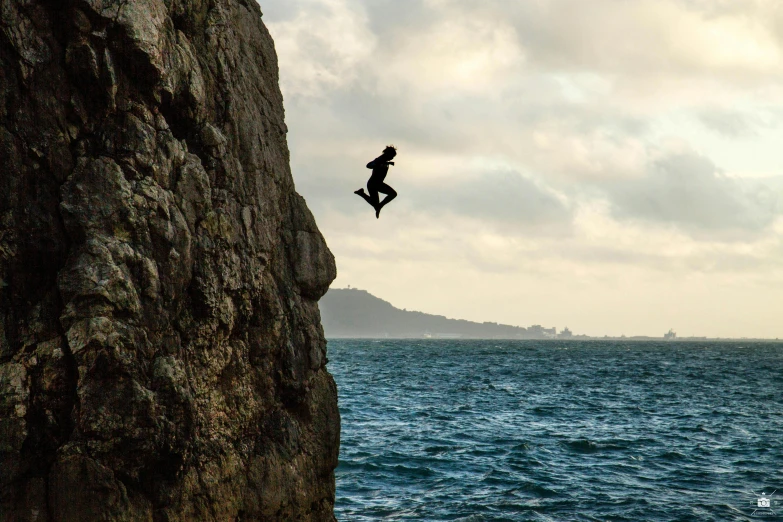 a person jumping off a cliff into the ocean, wellington, rock climbing, floating in the air, black