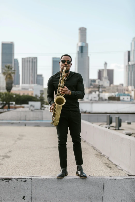 a man standing on top of a roof holding a saxophone, profile image, los angeles, will smith, riyahd cassiem