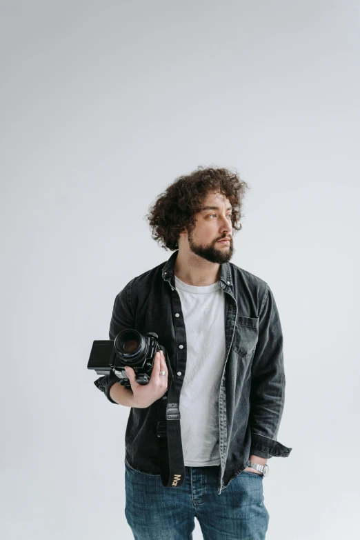 a man standing with a camera in his hand, curly haired, in front of white back drop, zachary corzine, over his shoulder