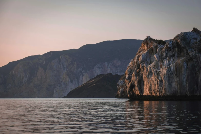 a large rock in the middle of a body of water, by Alexander Fedosav, pexels contest winner, romanticism, sheer cliffs surround the scene, evening light, greek nose, slide show