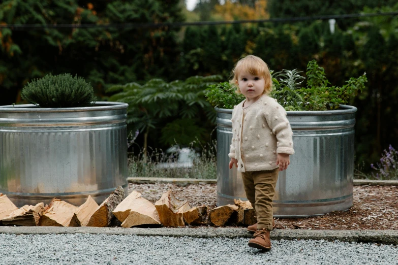 a little boy standing in front of a pile of wood, inspired by Elsa Beskow, unsplash, cardigan, gardens, grey, soup