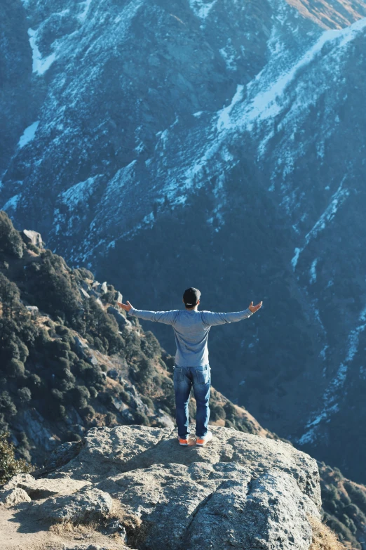 a man standing on top of a mountain with his arms outstretched, a picture, inspired by Michael Komarck, trending on unsplash, uttarakhand, top of a canyon, facing away from camera, on a sunny day