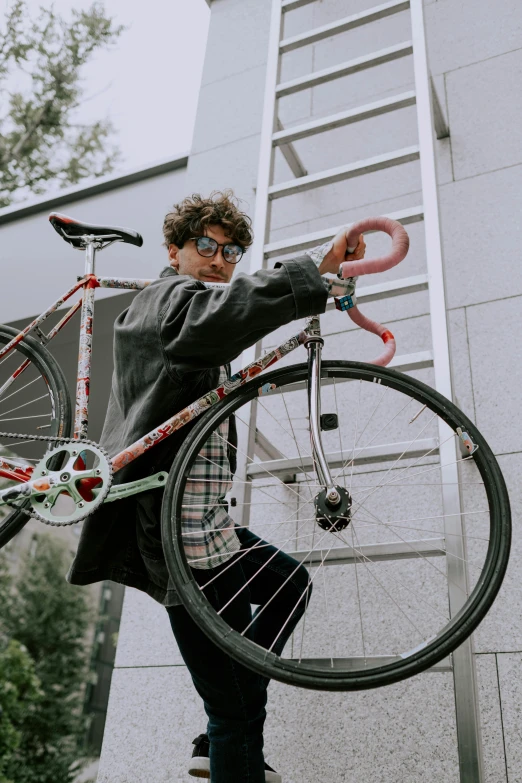 a man holding a bicycle up to the side of a building, with a curly perm, bad bunny, student, profile image