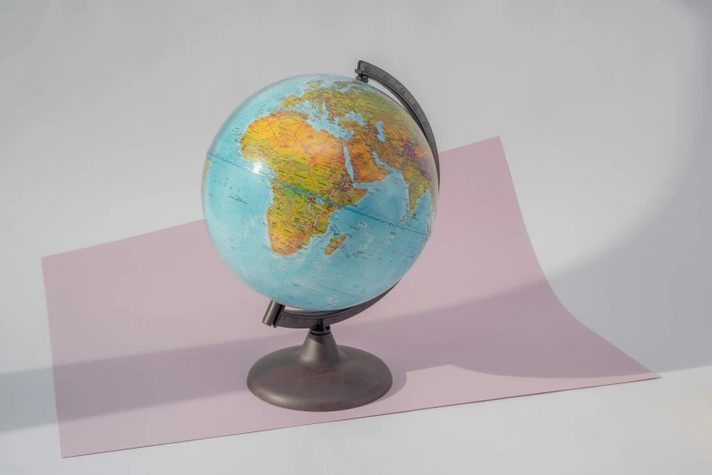 a small globe sitting on top of a piece of paper, textured base ; product photos, multi - coloured, grey, modeled