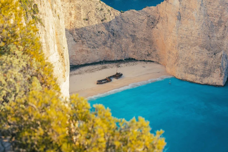 a boat sitting on top of a sandy beach next to a cliff, blue water, avatar image, greek, gigapixel photo