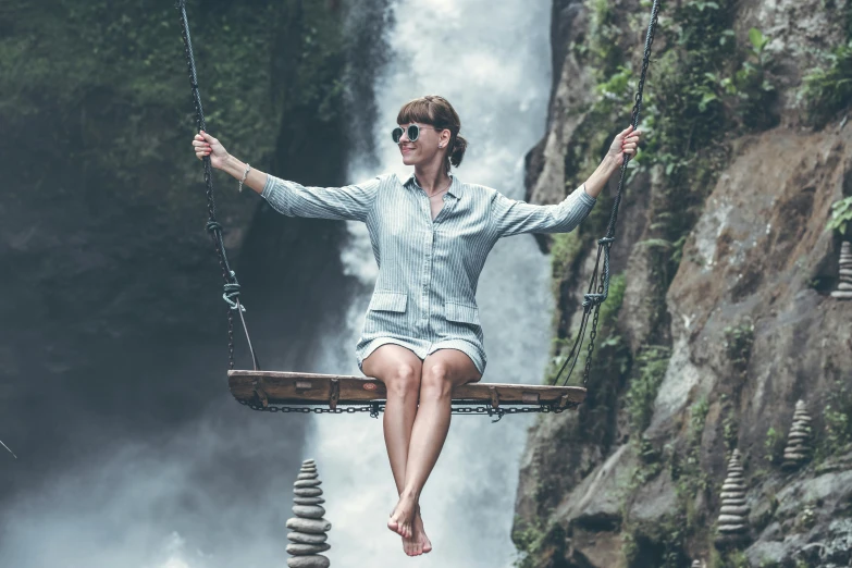 a woman sitting on a swing in front of a waterfall, pexels contest winner, playful smirk, grey, avatar image, flying shot