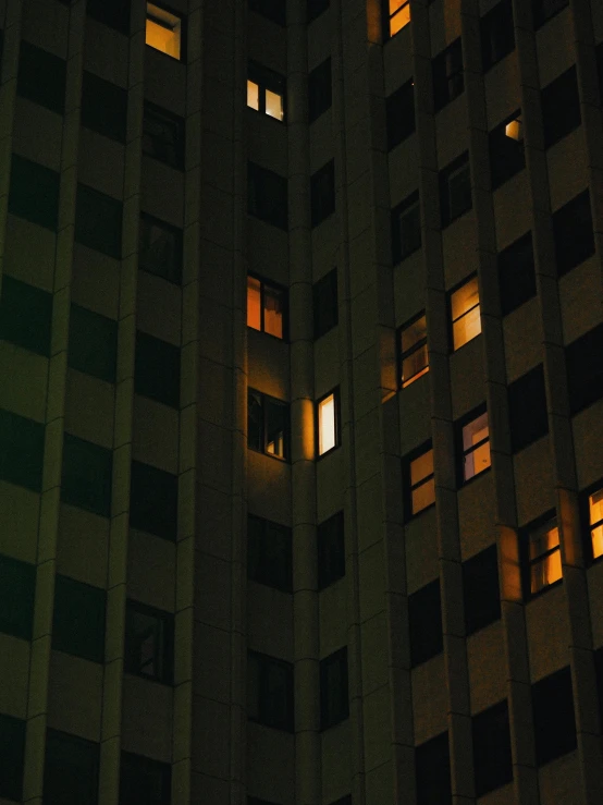 a tall building with windows lit up at night, a photo, inspired by Elsa Bleda, unsplash contest winner, beige and dark atmosphere, looking sad, golden windows, ignant