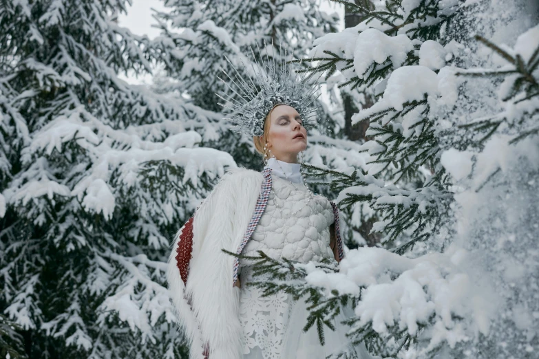 a woman in a white dress is standing in the snow, an album cover, inspired by Apollinary Vasnetsov, pexels contest winner, wearing intricate fur armor, on trees, model wears a puffer jacket, tilda swinton