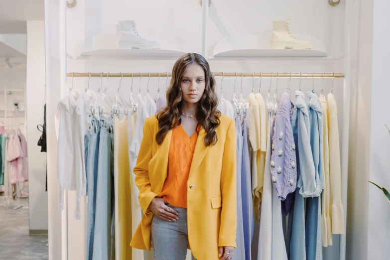 a woman standing in front of a rack of clothes, yellow details, aurora aksnes, photo for a store, orange jacket