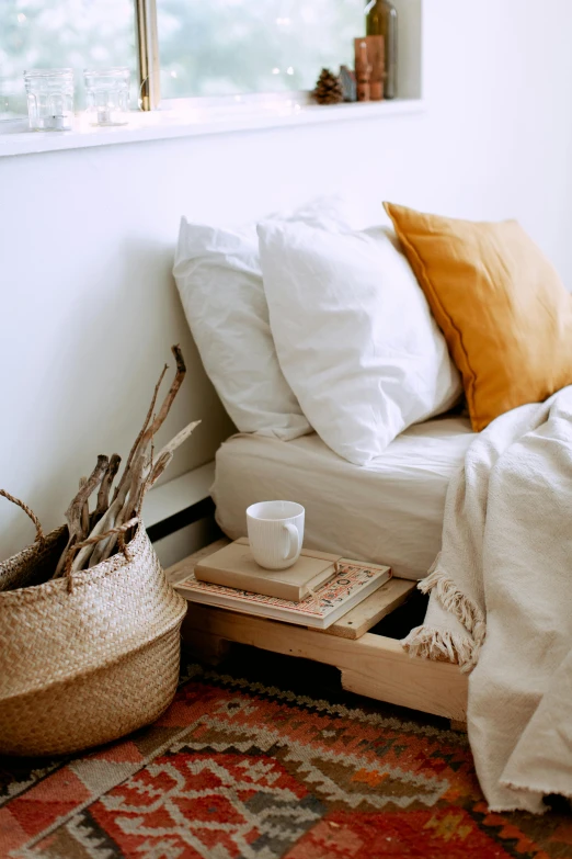 a bed sitting in a bedroom next to a window, inspired by Elsa Bleda, trending on pexels, wooden crates, some sandy yellow pillows, morning coffee, botanicals