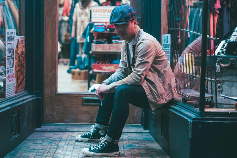 a man sitting on a bench in front of a store, pexels contest winner, blue fedora, wearing red converse shoes, natural lights, looking off to the side