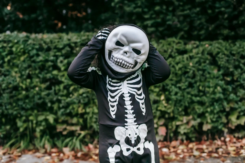 a little boy dressed up in a skeleton costume, a cartoon, by Nina Hamnett, pexels contest winner, balaclava covering face, wearing a round helmet, vantablack gi, fleshy skeletal