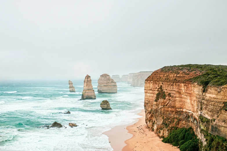 a group of people standing on top of a beach next to the ocean, a tilt shift photo, by Liza Donnelly, pexels contest winner, australian tonalism, sheer cliffs surround the scene, lined up horizontally, travelling through misty planes, photo of a beautiful