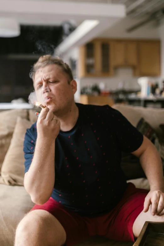 a man sitting on a couch smoking a cigarette, a portrait, featured on reddit, an overweight, limmy, blowing out smoke, lgbtq