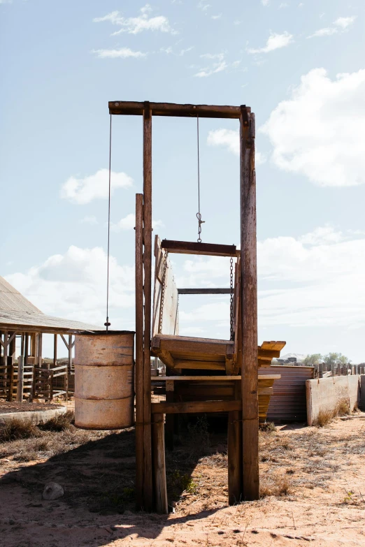 a wooden chair sitting on top of a dirt field, watertank, guillotine, hanging beef carcasses, outback