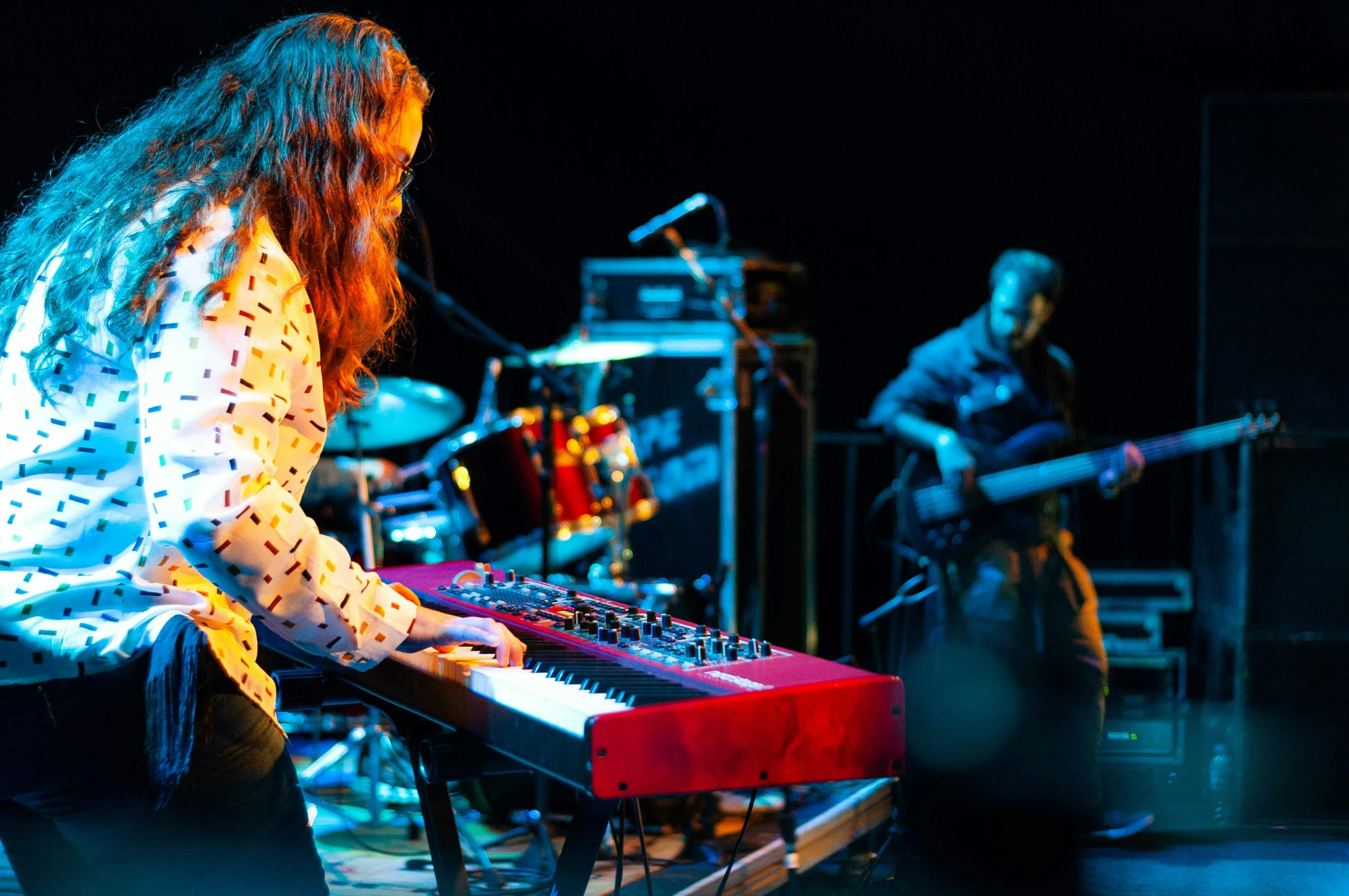 a woman standing next to a keyboard on a stage, pexels, antipodeans, brightly colored, band playing, reds, “ iron bark