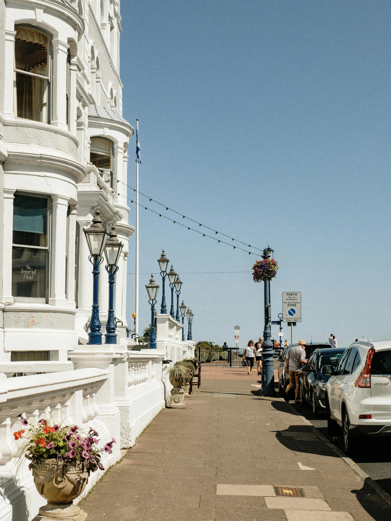 a white car parked on the side of a road, by Rachel Reckitt, unsplash, seaside victorian building, people walking around, lampposts, balcony