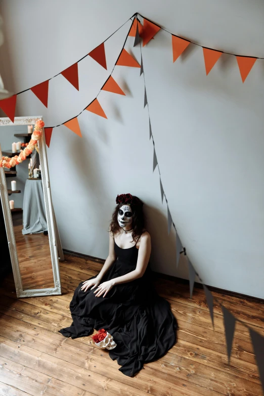 a woman sitting on the floor in front of a mirror, day of the dead, dark grey and orange colours, halloween theme, on a pale background