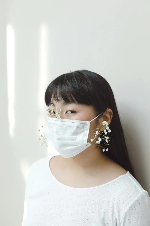 a woman standing against a wall wearing a face mask, by Ayami Kojima, earring, floeers in hair, made of lab tissue, white color