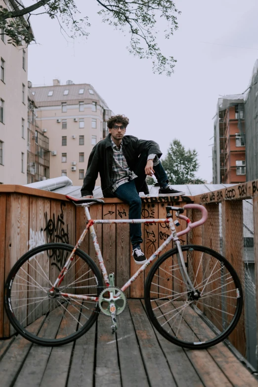 a man sitting on top of a wooden fence next to a bike, posing for a picture, dasha taran, college, profile image