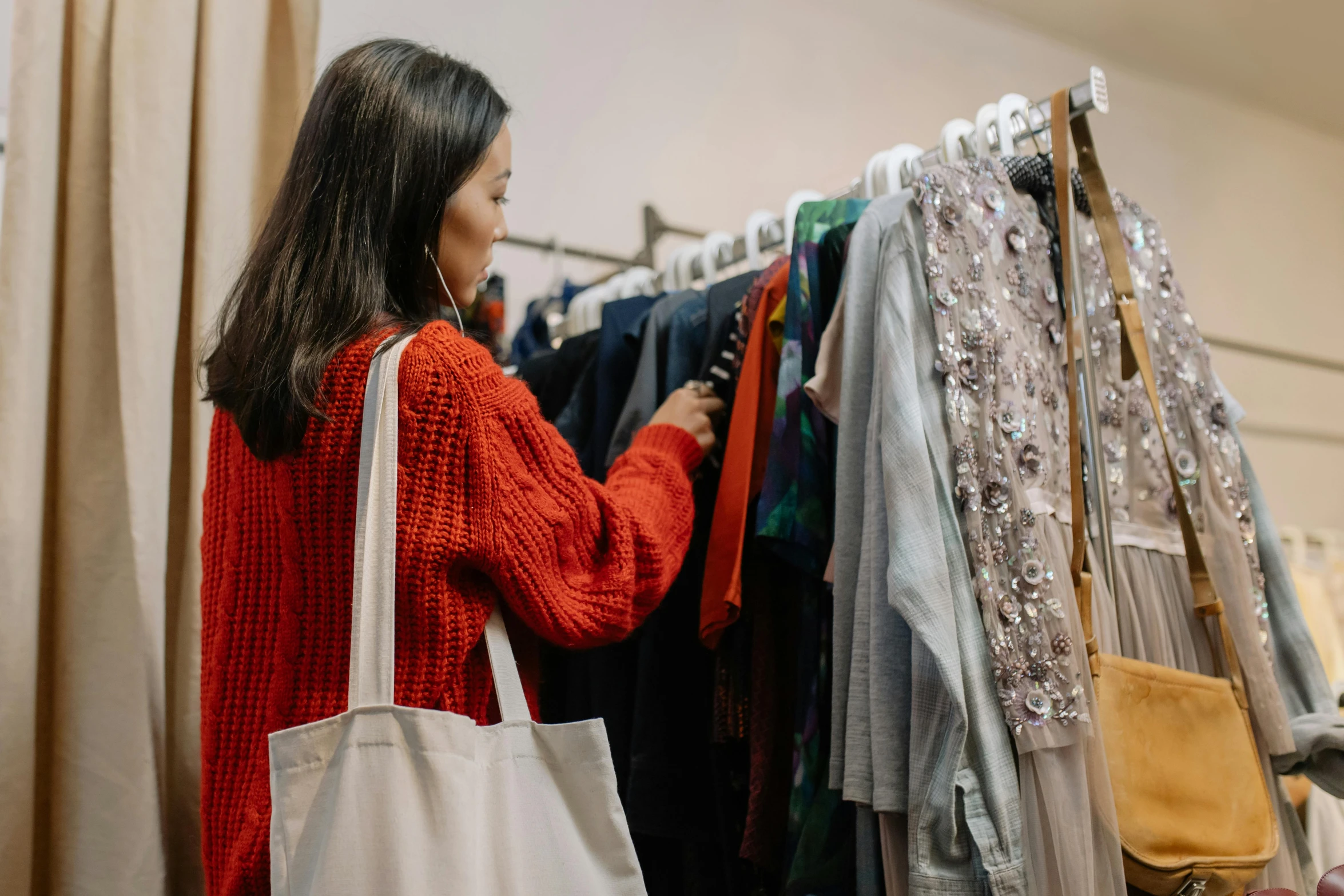 a woman standing in front of a rack of clothes, trending on pexels, dressed in red paper bags, inspect in inventory image, 🦩🪐🐞👩🏻🦳, red sweater and gray pants