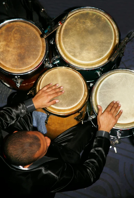 a group of people that are playing drums, overhead shot, real congas, hands shielding face, half turned around