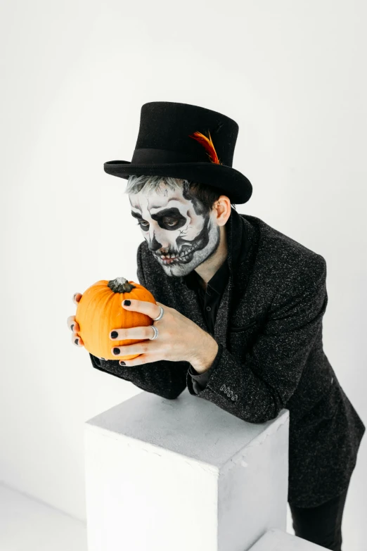 a man dressed as a skeleton holding a pumpkin, by Emma Andijewska, pexels contest winner, black top hat, with a white background, with grey skin, handsome man