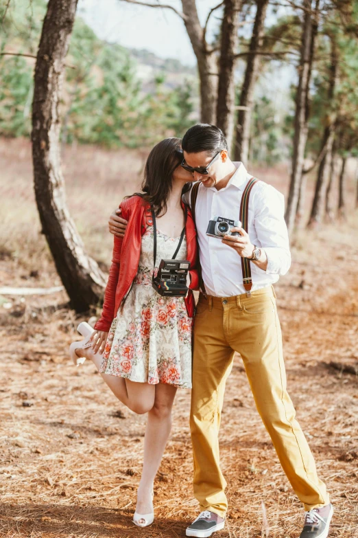 a man standing next to a woman holding a camera, a picture, trending on pexels, romanticism, in beautiful woods, vintage clothing, flirty, couple kissing