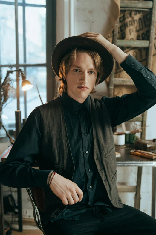 a man sitting in a chair wearing a hat, an album cover, inspired by August Sander, trending on pexels, renaissance, jamie campbell bower, cowboy portrait male, young man with medium - length, portrait androgynous girl