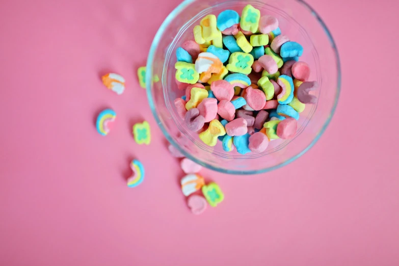 a bowl of conversation hearts on a pink surface, a cartoon, by Adam Marczyński, pexels, inside a glass jar, rainbow coloured rockets, clover, edible