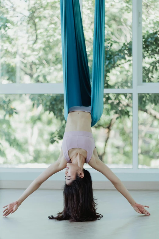 a woman doing a handstand in front of a window, by Yosa Buson, arabesque, lush gardens hanging, bangkok, relaxed. blue background, aerial silk