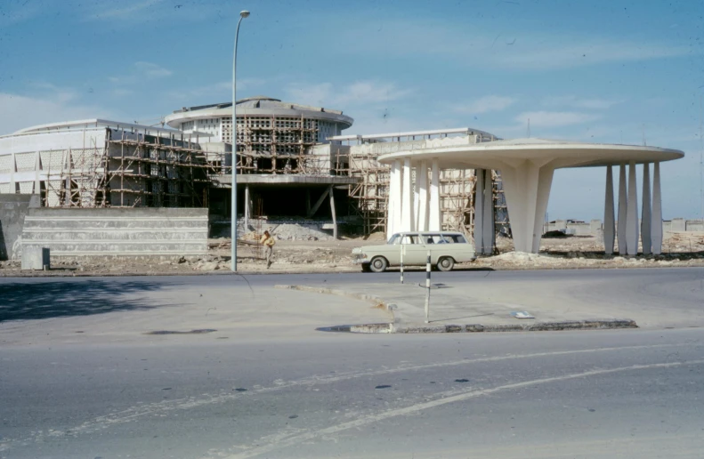 a car parked in front of a building under construction, brutalism, persian style architecture, gulf, brown, afar