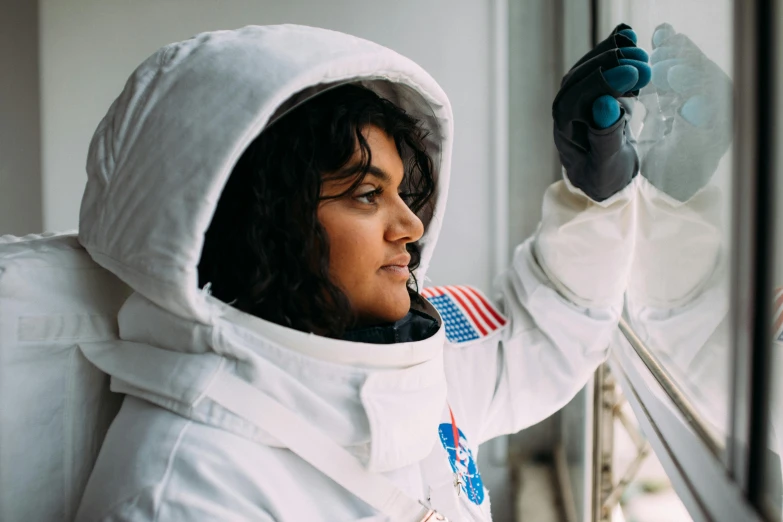 a woman in an astronaut suit looking out a window, pexels contest winner, imaan hammam, female camila mendes, portrait n - 9, - 9