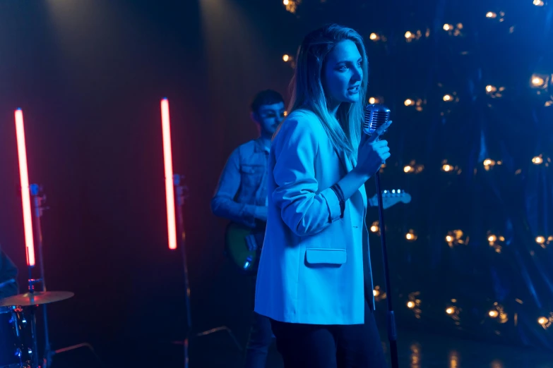 a woman standing on top of a stage holding a microphone, pexels, cinematic blue lighting, still image from tv series, heartbreak, band playing