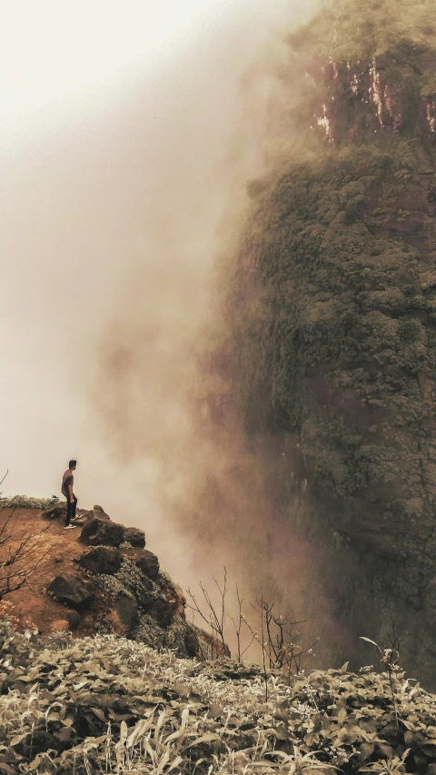 a man standing on top of a lush green hillside, a picture, pexels contest winner, romanticism, during sandstorm, (waterfall), grey, brown