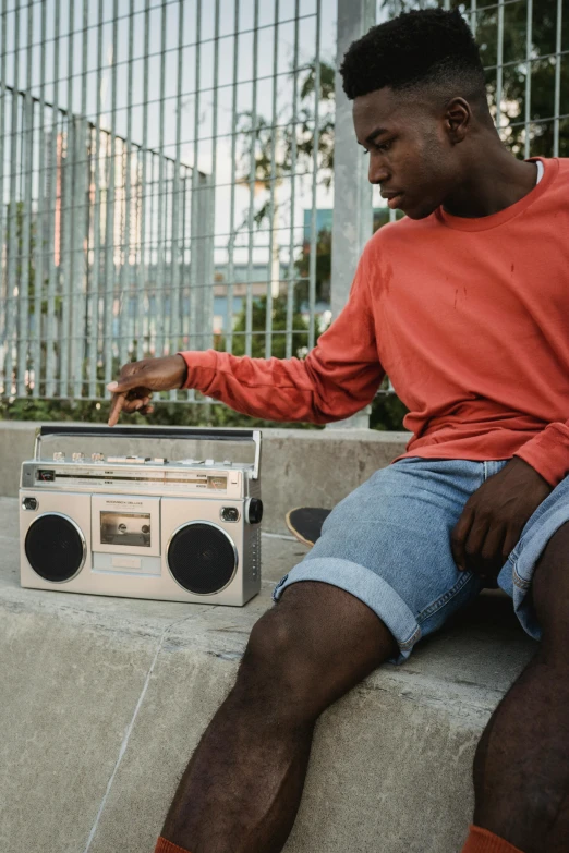 a man sitting on top of a cement wall next to a boombox, on a wooden table, calmly conversing 8k, product shot, block party