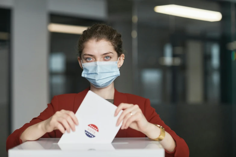 a woman wearing a face mask putting a vote in a box, pexels contest winner, renaissance, confident smirk, on desk, woman holding sign, zac retz