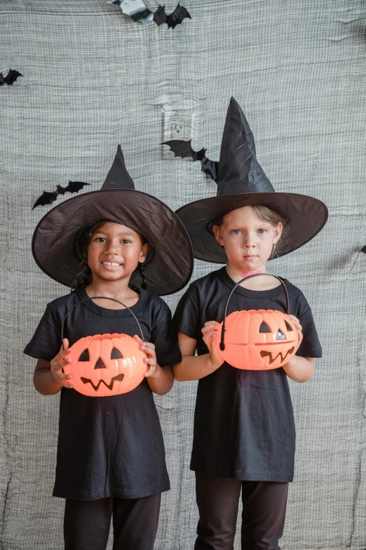 two children dressed in halloween costumes holding pumpkins, inspired by Kate Greenaway, pexels, happening, pointed black witch hat, square, blank, indoor picture