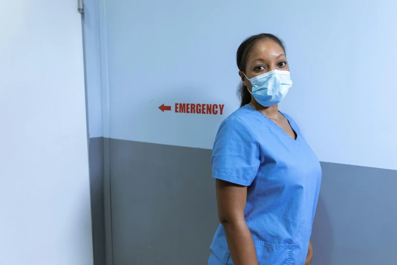 a woman in scrubs stands in front of an emergency sign, by Ella Guru, pexels contest winner, happening, avatar image, maria borges, profile image, hospital room