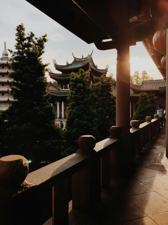 a person standing on a balcony in front of a building, inspired by An Zhengwen, unsplash contest winner, temple in the distance, beautiful late afternoon, lush surroundings, taken in the late 2000s