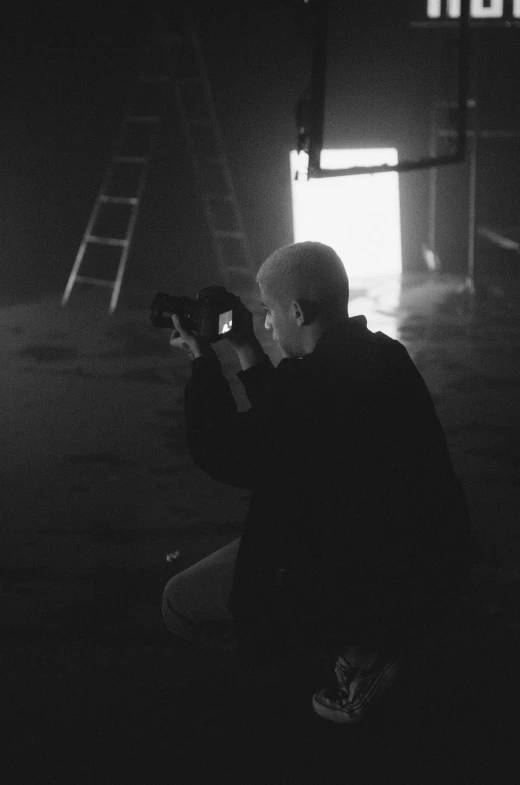 a black and white photo of a man holding a camera, inspired by Peter Lindbergh, in a dark warehouse, bts, light leak, paul barson