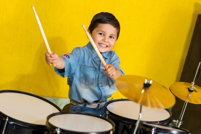 a young boy playing drums in front of a yellow wall, pexels contest winner, looking happy, avatar image, 5 years old, softplay