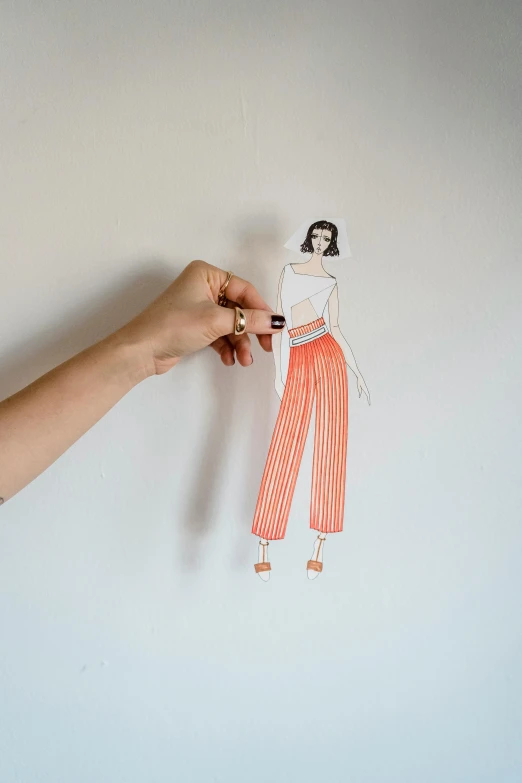 a person holding a paper cutout of a woman, a drawing, by Arabella Rankin, trending on pexels, interactive art, stripey pants, orange details, fashion studio, top down drawing