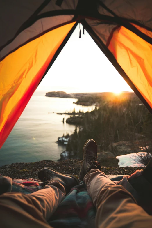 a person laying in a tent looking out at the ocean, large twin sunset, climbing up a cliffside, lake setting, adventure gear